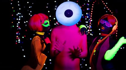 Wall Mural - two female gogo ravers in fluorescent costume dancing with masked man in disco setting