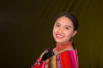 Beautiful hispanic model wearing andean traditional clothing smiling and posing for camera, dark yellow background