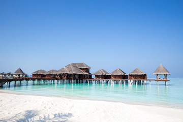 Wall Mural - Over Water Bungalows over crystal clear blue ocean sea water with white sand beach