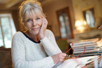 Senior woman sitting at desk and writing on book