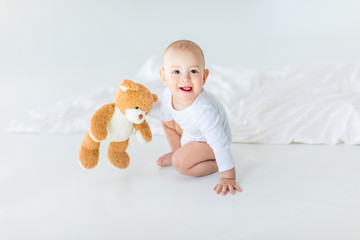 Portrait of adorable small baby boy with teddy bear playing on bed, 1 year old baby concept