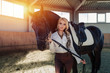 Beautiful elegant young blonde girl standing near her horse dressing uniform competition
