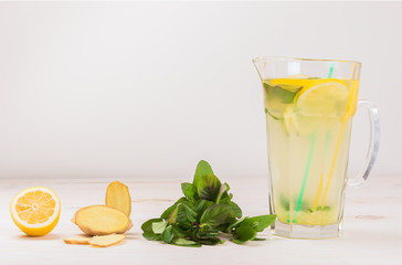 Wall Mural - A glass decanter with a summer refreshing lemonade made of lemons and ginger with mint added on a white wooden background. Detox water. Ingredients. Cleaning the body of toxins, vitamins