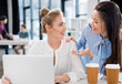 © LIGHTFIELD STUDIOS - Smiling young businesswomen using laptop and talking at workplace