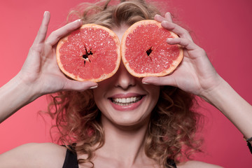 portrait of woman holding pieces of grapefruit isolated on pink