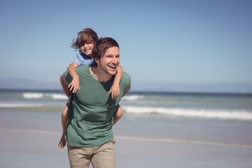 Wall Mural - Happy young father piggybacking his son at beach