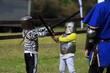 Dwaj mali chłopcy w zbrojach rycerskich walczą na miecze.