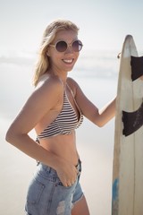 Wall Mural - Portrait of smiling young woman holding surfboard at beach