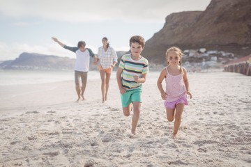 Wall Mural - Siblings running on sand with parents in background