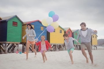 Wall Mural - Happy family holding balloons while running at beach