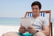 © WavebreakMediaMicro - Man sitting on sunlounger and using digital tablet on the beach
