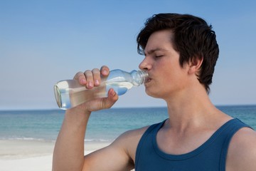 Wall Mural - Man drinking water from bottle at beach