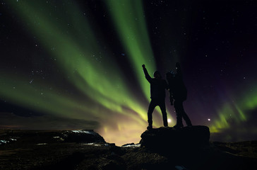 Wall Mural - silhouette two man standing on the rock with aurora borealis on the night sky, aurora hunting