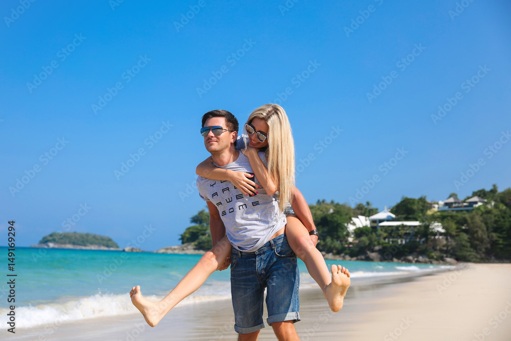 Young beautiful happy couple having fun on the beach. Piggyback rides ...