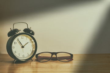 Alarm clock and glasses on wooden table.