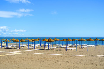 Wall Mural - Summer holiday view of a Mediterranean beach prepared for a tourist season, a sandy beach by the blue sea, deckchairs, straw umbrellas and a wooden path at Torremolinos resort on Costa del Sol, Spain.