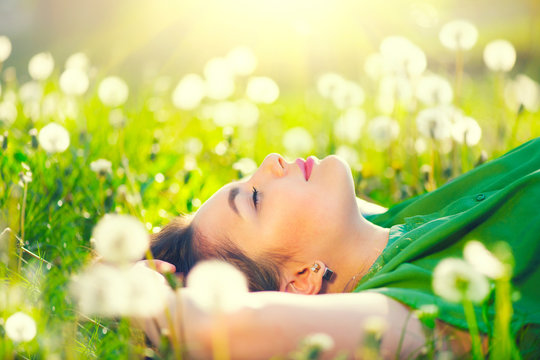 beautiful young woman lying on the field in green grass and dandelions