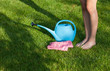 Barefoot woman standing on a freshly cut lawn , watering can and gloves 