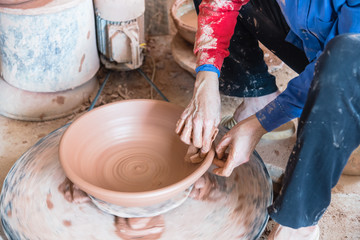 Close-up female hands throwing pottery on the wheel in a clay studio at ceramic village in Vietnam. Hand making, forming clay pot on pottery plate. Artisan making traditional ceramic manually.