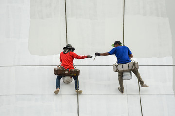 Un safety Painters and harnesses hanging high building in construction site,hand brush color work concept