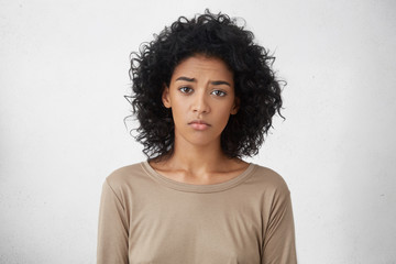 Attractive upset young dark skinned lady with Afro hairstyle feeling sad or bored expression while spending weekend at home, looking unhappy after friends forgot to invite her to party. Horizontal