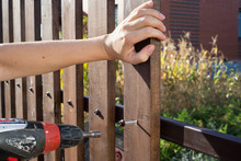 Close Up Of Hand Screewing Wood Plank To Metal Construction. Building A Wooden Fence With A Drill And Screw.