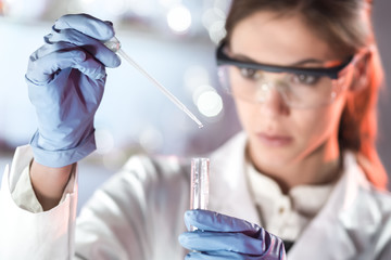 Poster - Life scientists researching in laboratory. Focused female life science professional pipetting solution into the glass cuvette. Lens focus on researcher's eyes. Healthcare and biotechnology concept.