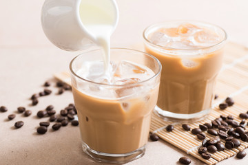 Pouring fresh milk into glass of ice coffee