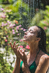 Wall Mural - Woman taking shower outside in tropical green Bali garden with a lot flowers. Fresh splashes of clean water. Luxury spa