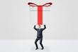 © gearstd - A small businessman holding a giant gift box with both hands above his head.