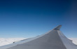 Airplane Wing Flying Above Clouds. Plain Blue Sky Background