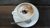 Hot mocca cofee in a cup with spoon and white dish, placed on wooden table