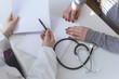 Doctor and patient are discussing about diagnosis. Medical doctor on white background holding a stethoscope, looking at medical form and taking notes.