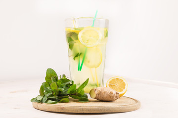 Wall Mural - A glass decanter with a summer refreshing lemonade made of lemons and ginger with mint added on a white wooden background. Detox water. Ingredients. Cleaning the body of toxins, vitamins