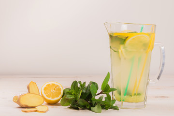 Wall Mural - A glass decanter with a summer refreshing lemonade made of lemons and ginger with mint added on a white wooden background. Detox water. Ingredients. Cleaning the body of toxins, vitamins