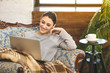 © denis_vermenko - Enjoying time at home. Beautiful young smiling woman working on laptop and drinking coffee while sitting in a big comfortable chair at home