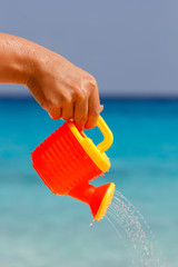 Wall Mural - Female hand pours water from a children's plastic watering can. Andaman sea, Similan Islands