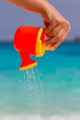 Wall Mural - Female hand pours water from a children's plastic watering can. Andaman sea, Similan Islands