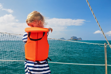 Happy little baby in life jacket on board of sailing boat watching offshore sea and tropical islands on summer cruise. Children travel adventure on family vacation. Safety during yachting with kids.
