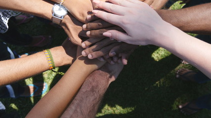 Arm of all races and colors stacked together one by one in unity and teamwork and then raised. Many multiracial hands getting together in the center of a circle and then cheer. Close up outdoor shot