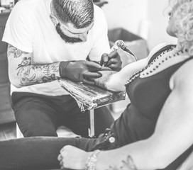 Wall Mural - Professional bearded tattoo artist making tattoo in his own ink studio on young blond woman