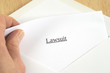 © dan_alto - Lawsuit printed on white paper and envelope, hand holding it, wooden background