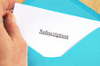 Subscription printed on white paper and blue envelope, hand holding it, wooden background