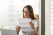 © fizkes - Businesswoman reading document while working in office. Young pretty female office worker attentively examining business letter. Confident woman entrepreneur analyzing recommendations of job applicant