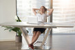 © fizkes - Successful businesswoman relaxing in chair with hands behind head. Female office head resting at large desk with laptop on it. Cheerful girl dreaming at work. Satisfaction from great job done concept