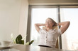 © fizkes - Cheerful woman sitting at desk with hands behind head. Business lady imagines happy future with closed eyes. Relaxed girl resting in office chair. Great pleasure from business success concept