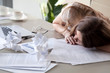 © fizkes - Tired woman sleeping at workplace covered crumpled papers. Overworked female entrepreneur give up after hard day and dozing at desk. Stressed businesswoman lying on table with documents under her head
