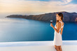 © Maridav - Luxury hotel terrace. Europe destination summer vacation. Asian woman drinking red wine relaxing enjoying view of the mediterranean sea in Oia, Santorini, Greece. Honeymoon high end travel holiday.
