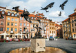 © bortnikau - Birds of pigeons are flying through Stare Miasto Old Town Market Square with Mermaid Syrena Statue in the center of Warsaw, Poland.