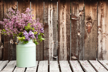 Large Bouquet Of Lilacs In A Green Container On A Rustic Wooden Table.